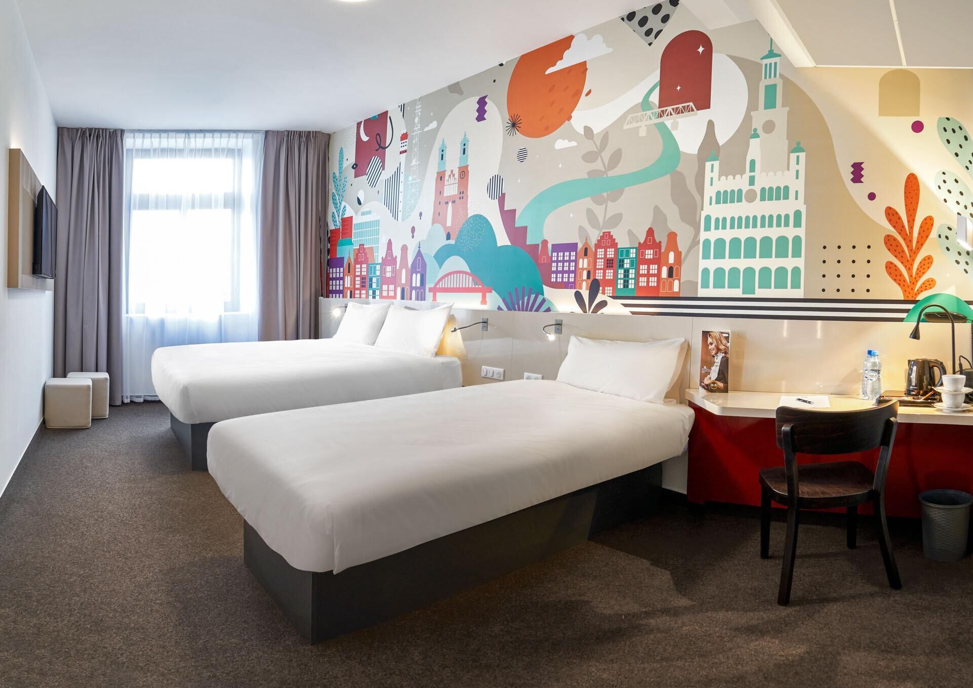 Une chambre d’hôtel avec deux lits, un bureau avec une chaise, une machine à café et une fresque murale.