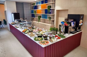 Uma mesa de buffet com diversos alimentos e uma máquina de café.