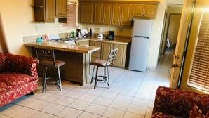 Cocina compacta con una isla central, dos taburetes de bar y un refrigerador.