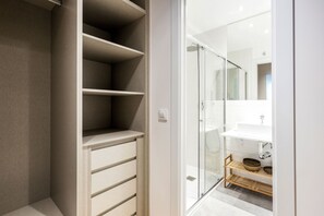 A modern bathroom with a glass shower enclosure, a white sink, and a wooden shelf with baskets.