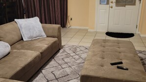 Ein Wohnzimmer mit einem beigefarbenen Sofa, passendem Hocker und einem gemusterten Teppich.