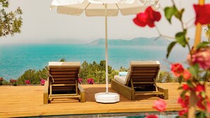 A wooden deck with two lounge chairs and a white umbrella, overlooking a clear blue sea and distant mountains. - Vista Del Amor Faralya (Fethiye)