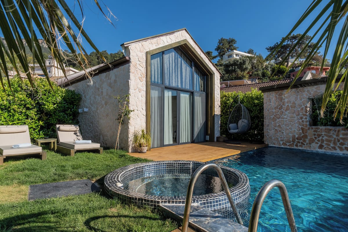 A stone building with a swimming pool, a wooden deck, and lounge chairs.