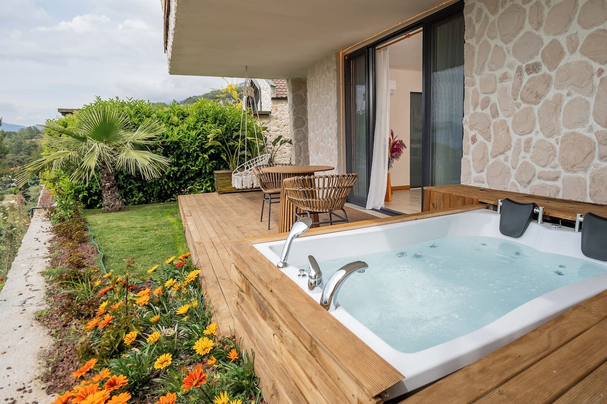 A hot tub with a wooden deck, stone wall, and outdoor furniture.