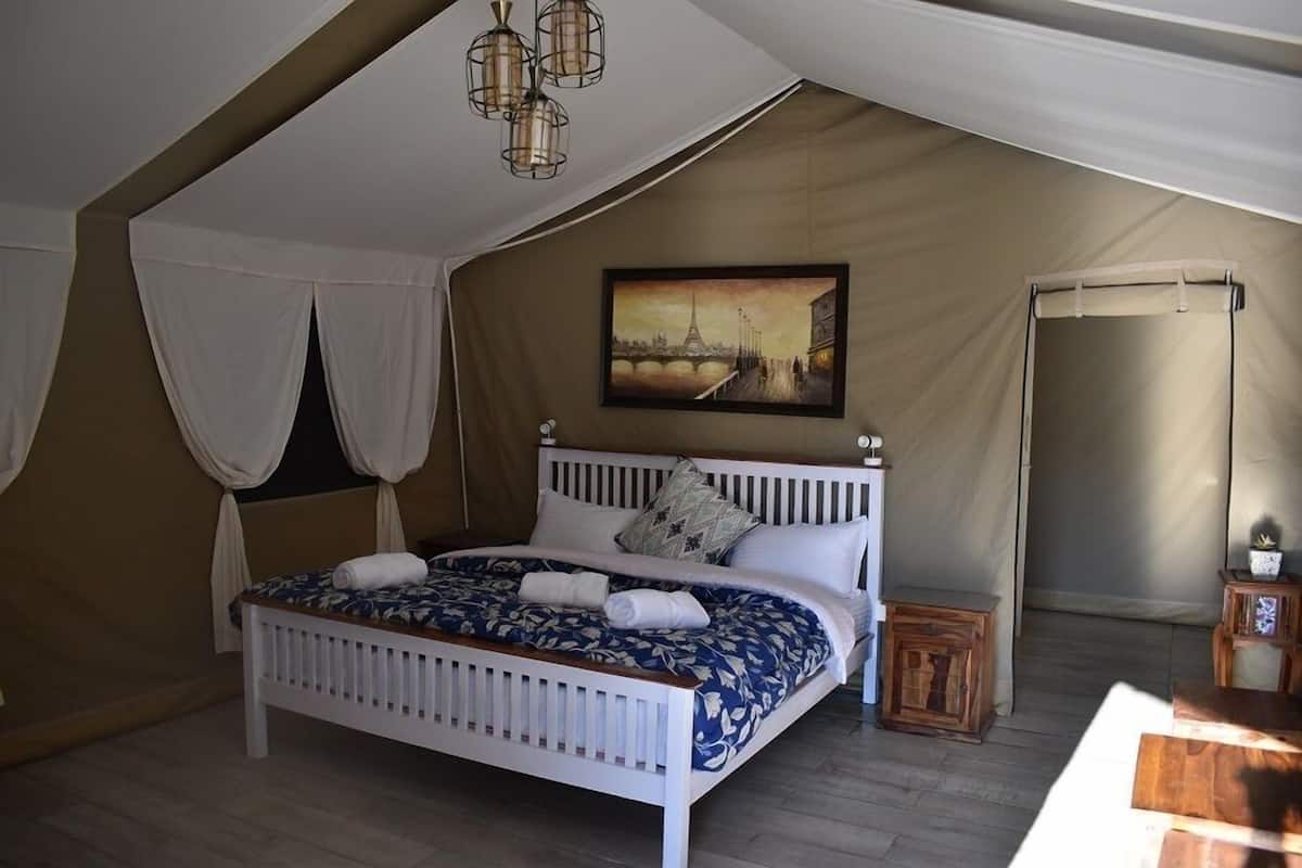 A bedroom with a white bed, a painting of a bridge, and a tent-like structure.