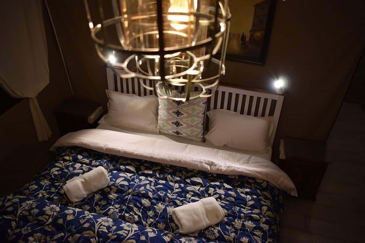 A neatly made bed with a floral-patterned bedspread, white pillows, and a decorative hanging light fixture above it.