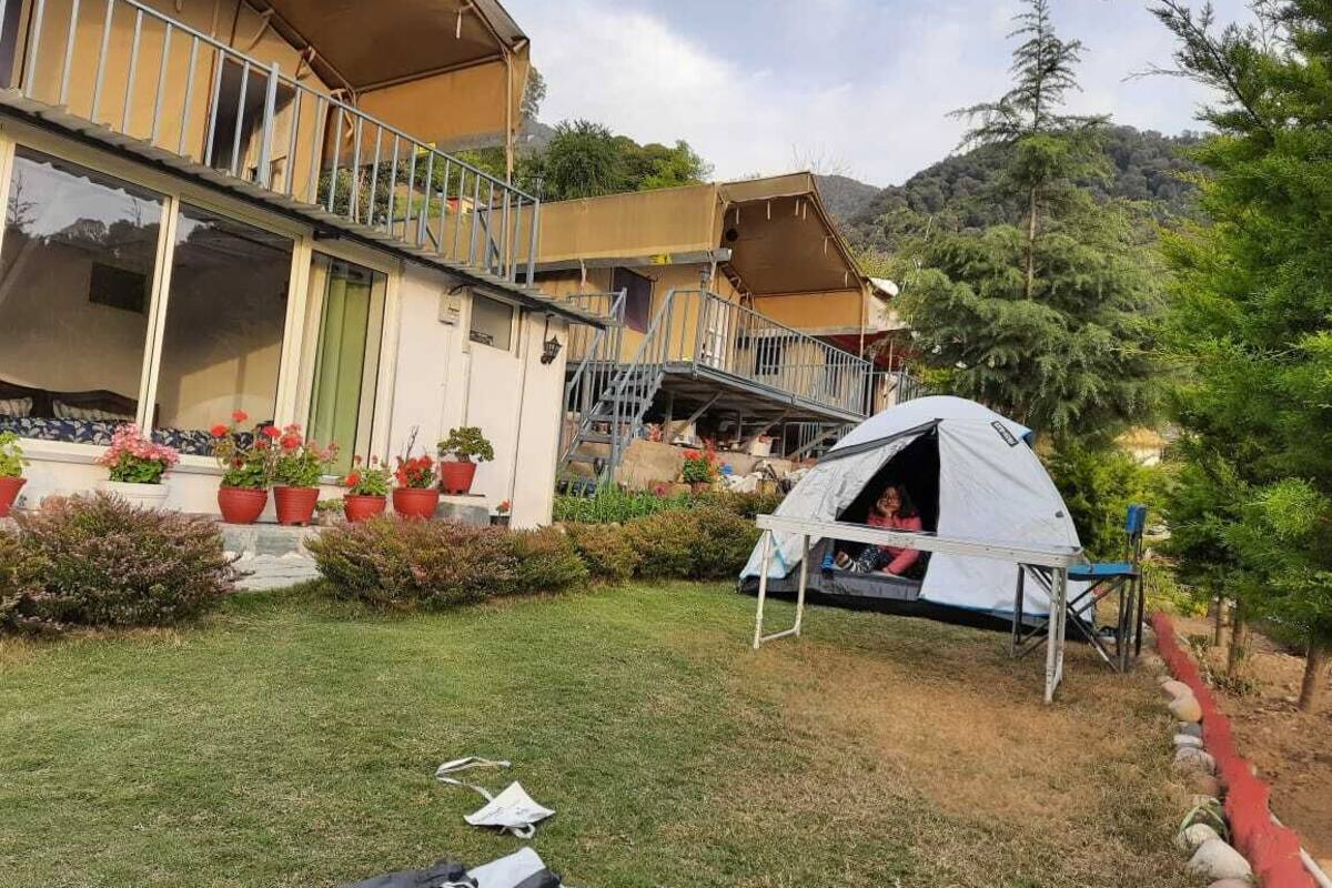 A two-story building with a balcony, a tent set up in the yard, and potted plants.