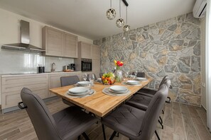 Cocina moderna con pared de piedra, mesa de comedor de madera y sillas grises.