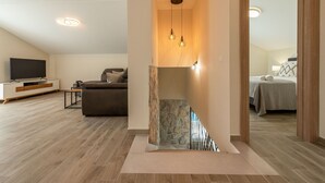 A modern living room with a flat-screen TV, a sofa, and a coffee table. A staircase with a wooden railing leads to a bedroom with a bed and a bathroom visible through an open door. - Villa Petar ZadarVillas (Donji Kašić)