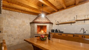 A stone fireplace with a wooden ceiling and a table with fruit and wine glasses in front. - Villa Petar ZadarVillas (Donji Kašić)