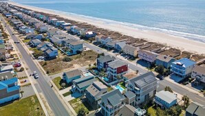 A coastal residential area with houses along the beach, a clear sky, and a road running parallel to the beach.