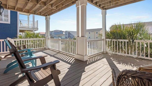 A covered outdoor deck with wooden furniture, white railings, and a view of residential buildings.