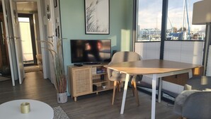 Una sala moderna con una mesa de comedor de madera, un televisor sobre un mueble bajo y un ventanal con vistas a barcos.