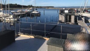 Un puerto deportivo con barcos amarrados, una zona cubierta con asientos y vistas al agua y la costa lejana.