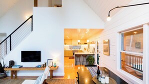 A modern kitchen with a central island, a dining area with a table and chairs, and a staircase leading to an upper level. - Mossybrook Hideout: Dog Friendly Oasis in High Falls w/ Hot Tub (High Falls)