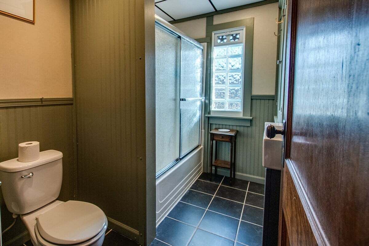 Ein Badezimmer mit Toilette, einem Fenster mit Milchglas und einem kleinen Holzschemel.