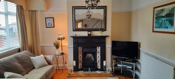 A living room with a fireplace, a sofa, a television, and a window with blinds. - Cosy and Stylish House on the Coast Near Liverpool (Wirral)