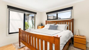 A bedroom with a wooden bed, a nightstand, and a window with a view of a building outside. - Back Beach Beauty in Smiths Beach (Smiths Beach)