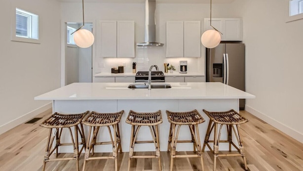 Uma cozinha moderna com armários brancos, uma ilha grande com banquetas, eletrodomésticos de aço inoxidável e iluminação pendente.