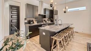 A modern kitchen with dark cabinetry, a marble island, and wicker bar stools. - 17- Home w/ Rooftop - The Music City Collection (Nashville)
