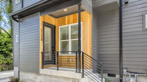 A modern house with a wooden porch, a black metal railing, and a stone base. - 18- Luxe Modern Home- The Music City Collection (Nashville)