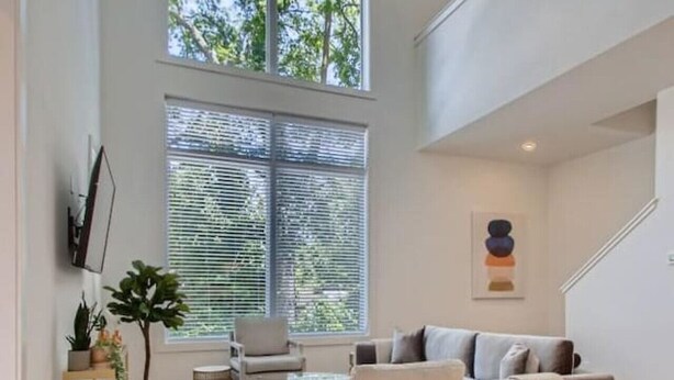 A spacious living room with a high ceiling, large windows, and a staircase. - 18- Luxe Modern Home- The Music City Collection (Nashville)
