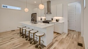A modern kitchen with a central island, bar stools, pendant lights, and white cabinetry. - 18- Luxe Modern Home- The Music City Collection (Nashville)