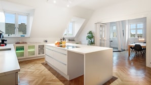 A modern kitchen with a central island, wooden herringbone flooring, and large windows providing natural light. - 250 Sqm Smack Bang in the Center of Copenhagen (Copenhagen)