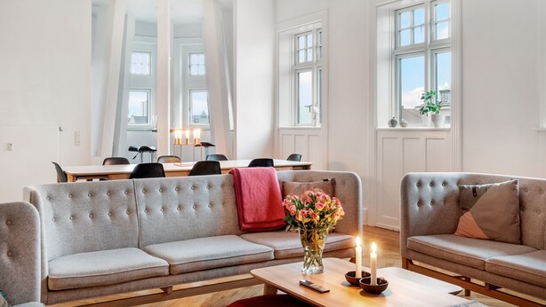 A modern living room with a grey sofa, a coffee table with a vase of flowers, and a dining area with a table and chairs. - 250 Sqm Smack Bang in the Center of Copenhagen (Copenhagen)