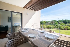 A dining area with a wooden table set for four, wicker chairs, and a view of a garden and trees. - Apart L'Orange - A Luxurious Vacation Retreat (Quarteira)