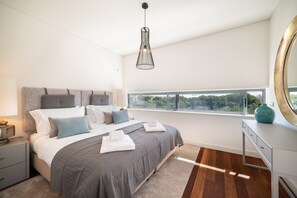 A modern bedroom with a large bed, a bedside table, a dresser, and a window with a view. - Apart L'Orange - A Luxurious Vacation Retreat (Quarteira)
