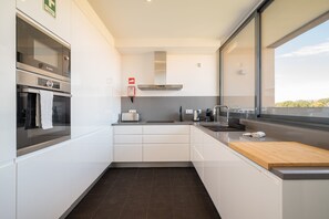 A modern kitchen with white cabinets, a stainless steel oven, a toaster, and a wooden cutting board. - Apart L'Orange - A Luxurious Vacation Retreat (Quarteira)