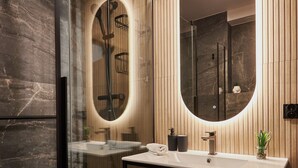 Un baño moderno con cabina de ducha de vidrio, tocador de madera con espejo y suelo estampado.