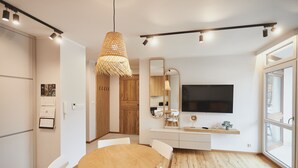 Una cocina moderna con una mesa redonda de madera, sillas blancas, un espejo grande y un televisor sobre el mostrador.