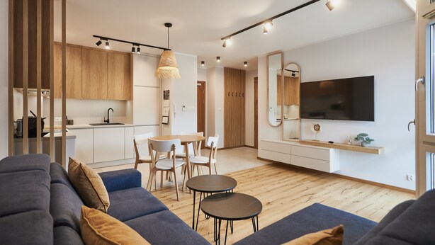 Una sala de estar moderna con sofá, mesa de comedor con sillas, zona de cocina y televisor montado en la pared.