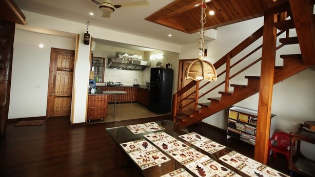 A spacious living area with a wooden staircase, a dining table with placemats, and a kitchen in the background. - Echor The Rustic Retreat Kasauli (Kasauli)