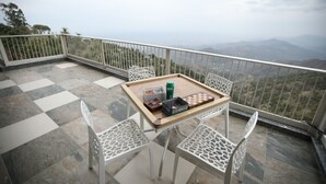 A balcony with a checkered floor, a table with a chessboard, chairs, and a railing overlooking a mountainous landscape. - Echor The Rustic Retreat Kasauli (Kasauli)