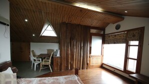 A room with a wooden ceiling, a dining area with chairs and a table, a bed with a patterned bedspread, and large windows with curtains. - Echor The Rustic Retreat Kasauli (Kasauli)