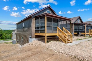 A modern building with large windows, a wooden deck, and a staircase leading to a second level. - 4BD Spacious Group Retreat Near Table Rock Lake + Boat Launch | Baxter Boat House (Lampe)