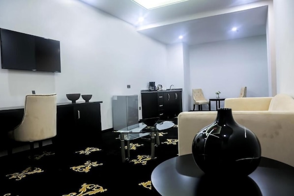 Uma sala de estar moderna com um sofá, uma mesa de centro de vidro, um vaso preto e uma televisão de tela plana na parede.
