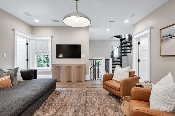 Una sala moderna con un sofá, sillones, un televisor de pantalla plana y una escalera.