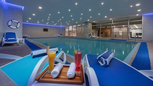 Zona de piscina con sillones de descanso, toallas y una bandeja con bebidas y fruta decorativa.
