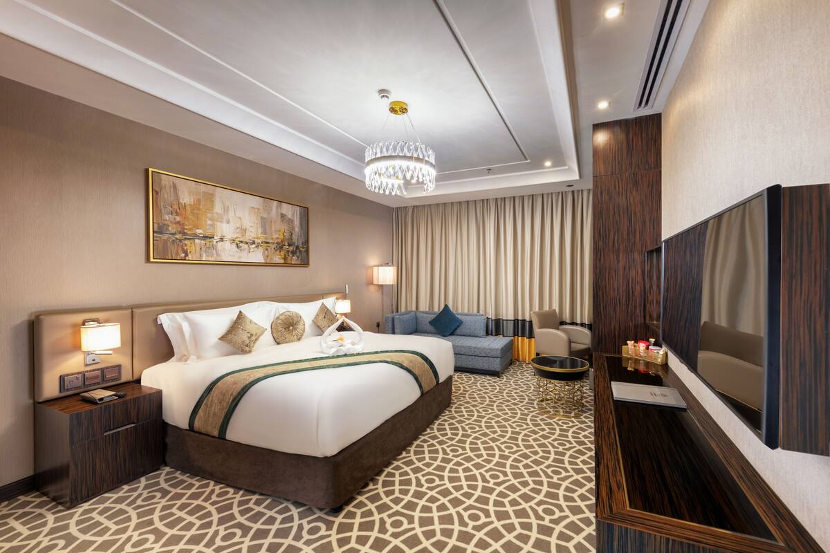 Ein Hotelzimmer mit einem großen Bett, einem Fernseher, einem Schreibtisch und einer Chandelier.