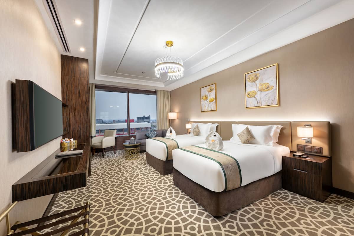 Ein Hotelzimmer mit einem großen Bett, zwei Nachttischen, einem Fernseher, einem Schreibtisch, einem Sessel und Blick auf die Stadt.