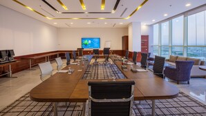 Un salón de conferencias con una larga mesa, sillas, una pantalla de televisión y vistas a la ciudad a través de amplias ventanas.