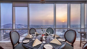 Comedor con una mesa dispuesta para seis personas, ventanas amplias con vistas a la ciudad y una vista del atardecer.