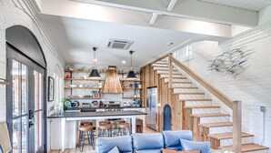 A modern kitchen with wooden accents, a central island, and a staircase leading to an upper level. - Carlton Landing-The Coral Cottage (Carlton Landing)