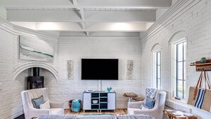 A living room with a large grey sofa, two armchairs, a wooden coffee table, and a TV mounted on a white brick wall. - Carlton Landing-The Coral Cottage (Carlton Landing)