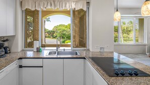 A modern kitchen with a built-in stove, a sink, and a window with a view of greenery. - Palms at Wailea #1605 Tropical Garden View Ground Floor, Wifi, Shared Hot Tub (Wailea)