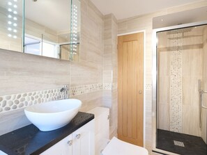A modern bathroom with a large white sink, a black countertop, a wooden door, and a glass shower enclosure.